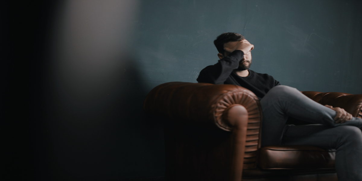 Image commercially licensed from https://unsplash.com/photos/a-man-holds-his-head-while-sitting-on-a-sofa-BuNWp1bL0nc